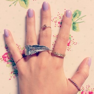 A picture of a hand wearing rings and Essie lilacism nail polish